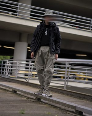Ein Mann in einem schwarz-grünen Techwear Outfit bestehend aus Arc'teryx Sinsolo Bucket Hat, Nemen Techwear Jacke, Nemen Techwear Shirt und ACRONYM P30A-DS Techwear Hose und Asics Techwear Sneaker