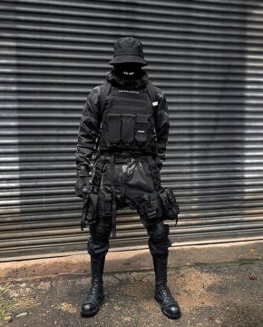 Ein Mann in einem komplett schwarzen Warcore Outfit mit Plattenweste, Magazintaschen, Warcore Hose mit viel Zubehör und Maske