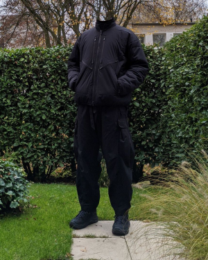 Eine Person stehend in einem Garten mit ACRONYM J91 Techwear Jacke, Nilmance Reversible Techwear Cargo und Hoka Tor Low Techwear Schuhen